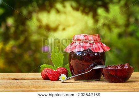 strawberry jam on table with sunshine blurred natural background. Preserved fruits. Homemade jam in jar covered with paper. Strawberry jam