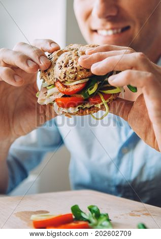 Man eats a big sandwich with meat and wegetables