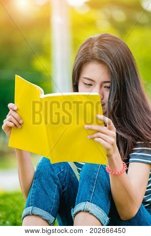 Asian teenage girl reading a book in the park on Sunday morning a brilliant weekend. The women students are reading book intended to prepare for university entrance exams.