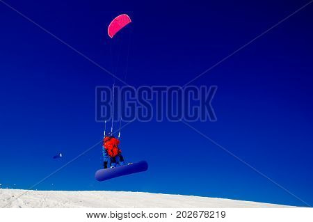 Snowboarder with a kite on fresh snow in the winter in the tundra of Russia against a clear blue sky. Teriberka, Kola Peninsula, Russia. Concept of winter sports snowkite.