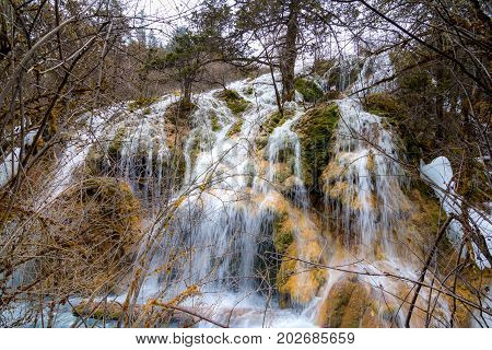 Waterfall in the forest. Stream of water on the rocks. Clean and cold water over the coniferous forest. Stones in the snow. Powerful rocks and a stream of water