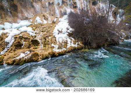 Waterfall in the forest. Stream of water on the rocks. Clean and cold water over the coniferous forest. Stones in the snow. Powerful rocks and a stream of water