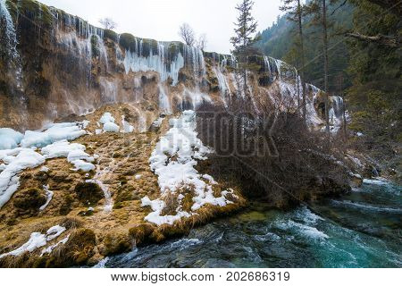 Waterfall in the forest. Stream of water on the rocks. Clean and cold water over the coniferous forest. Stones in the snow. Powerful rocks and a stream of water