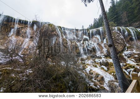 Waterfall in the forest. Stream of water on the rocks. Clean and cold water over the coniferous forest. Stones in the snow. Powerful rocks and a stream of water