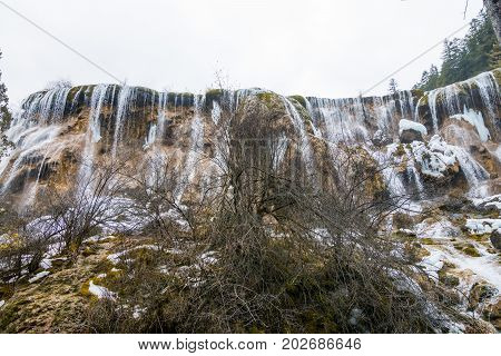 Waterfall in the forest. Stream of water on the rocks. Clean and cold water over the coniferous forest. Stones in the snow. Powerful rocks and a stream of water