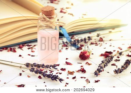 Glass corked bottle of pink perfumed water, book, dried lavender twigs, soft light shining, toned.