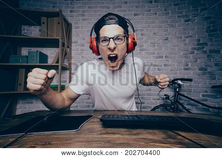 Young man playing game at home and streaming playthrough or walkthrough video. Shouting crazy guy has won his last and the hardest battle in vr. He is looking at camera with aggressively happy face expression shaking with one fist in front of it.
