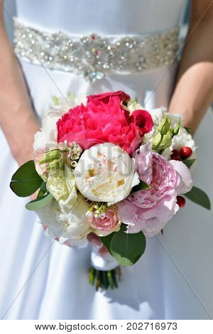 Beautiful bride is holding a wedding colorful bouquet. Beauty of colored flowers. Close-up bunch of florets. Bridal accessories. Female decoration for girl. Details for marriage and for married couple