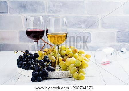 Red and white wine in glasses with grapes on white background. Assortment of autumn harvest beverages. Copy space
