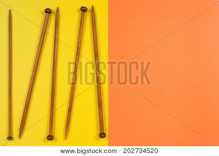 Variety of bamboo knitting needles in different sizes on yellow and orange background. Top view