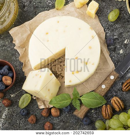 Young white cheese, a new recipe for cheese with fenugreek, a hard chopped Parmesan on a gray stone background with blueberries, nuts, green grapes, honey. Top view. Selective focus.