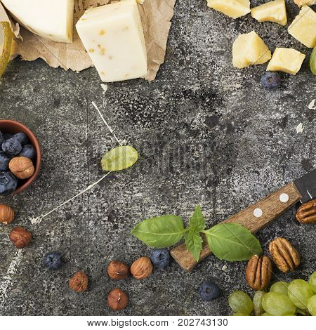 Young white cheese, a new recipe for cheese with fenugreek, a hard chopped Parmesan on a gray stone background with blueberries, nuts, green grapes, honey. Top view. Selective focus.
