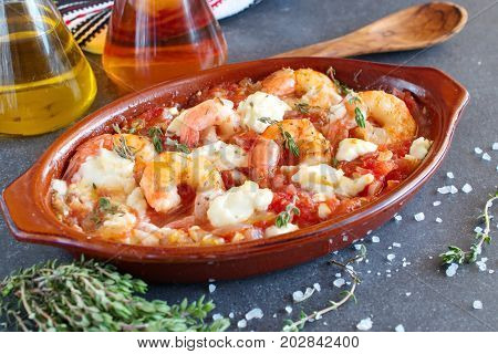Greek traditional food. Oven backed prawns with feta tomato paprika thyme in a traditional ceramic form on a abstract background. Healthy eating concept. Mediterranien lifestyle.