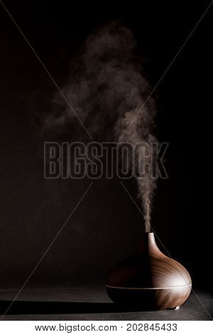Aromatherapy essential oil diffuser device working. Spa health treatment against black background with copy space.