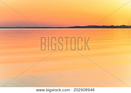 Uncomplicated evening sunset with beautiful sun glare on the water. A strip of coast on the horizon dark. Background blurred image.