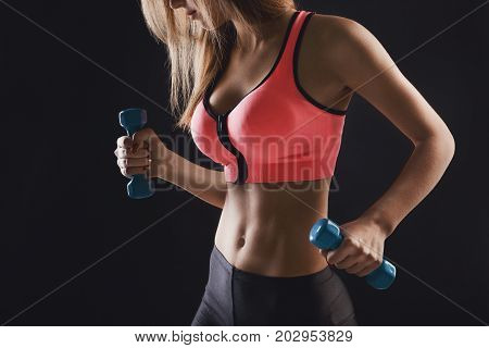 Fitness model woman with dumbbells on black studio background. Unrecognizable girl in fitwear with sport equipment. Bodybuilding, healthy lifestyle concept