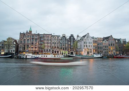 View Of Typical Amsterdam Houses Along Canal On Cloudy Sky.