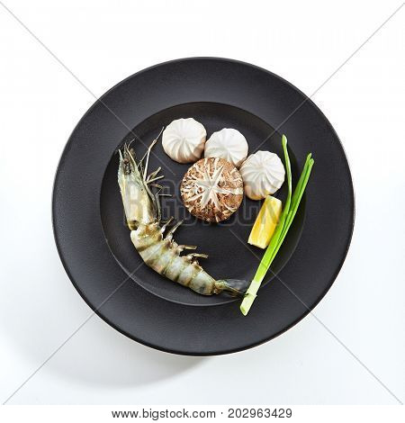 Teppanyaki Japanese and Korean Grill Food - 6/8 Shrimp with mushrooms with fresh herbs and slice of lemon on black plate. Raw products, preparation for frying on teppan. Top View