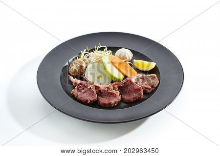 Teppanyaki Japanese and Korean Grill Food - Rack of lamb with vegetables and mushrooms with sprouts and lemon slice on plate on white  background. Preparation of raw products for frying on teppan