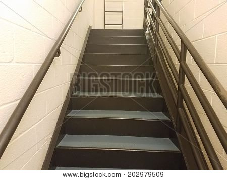 cement stairs in a stairwell with metal railing and white walls with ladder
