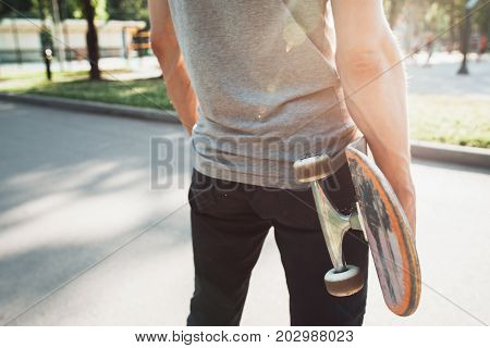 Unrecognizable young man with skateboard in hands. Waiting for next step of sport challenge and competition, short break and self-confidence. Skateboarding urban lifestyle and culture background