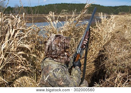 Duck Hunter With A Shotgun Hid In A Hunting Blind Of Reeds On The Lake