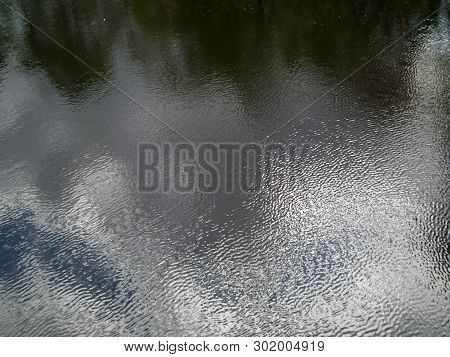 Water Covered With Ripples Creates A Beautiful Background. The Sky And The Trees Reflected In The Wa