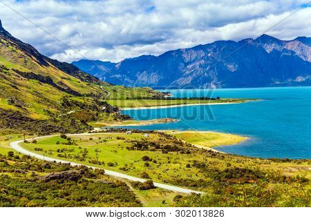Green grassy mountains surround the magnificent Hawea Lake. Journey to the ends of the world. South Island, New Zealand. The concept of ecological, active and photo tourism