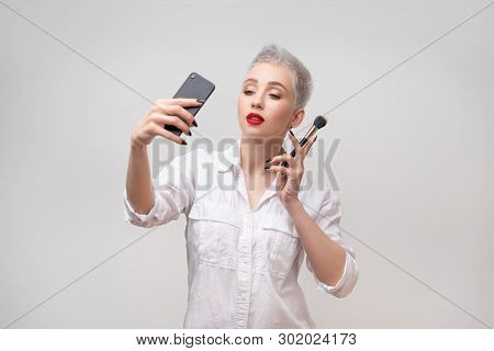 Studio Portrait Of Beautiful Trendy Girl With Short Hair Taking Selfie Via Cell Phone Over White Iso
