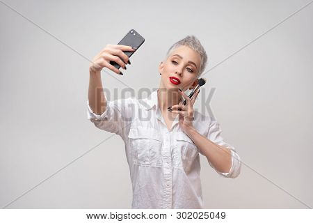 Studio Portrait Of Beautiful Trendy Girl With Short Hair Taking Selfie Via Cell Phone Over White Iso