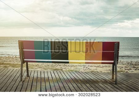 Rainbow Lgbt Pride Flag Painted On A Wooden Bench On The Beach With The Sea In The Background.