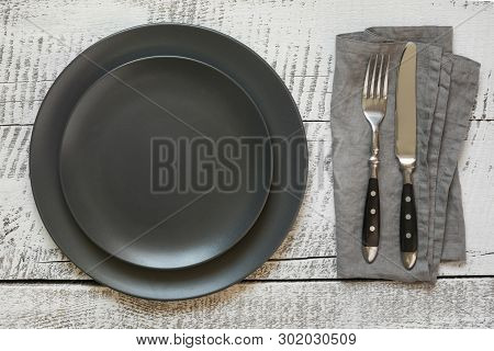 Table Place Setting With Black Plate On White Wooden Table. Top View.