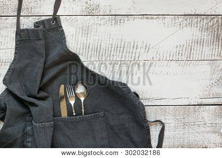 Gray Kitchen Apron With Silverware On Wooden Table. View From Above With Space For Text.
