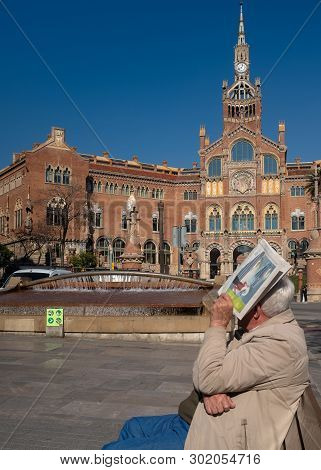 Barcelona, Catalonia / Spain - February-06-2019: An Elderly Man Is Sitting On A Bench And Covers His
