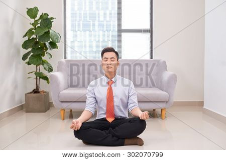 Businessman Meditating In Lotus Pose On The Floor In The Office