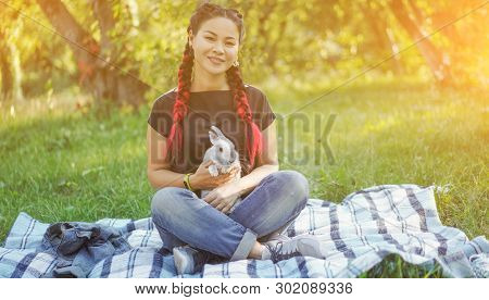 Cute Asian Woman On Picnic With Rabbit. Beautiful Woman With Braided Hair Hugging Her Bunny On Blank
