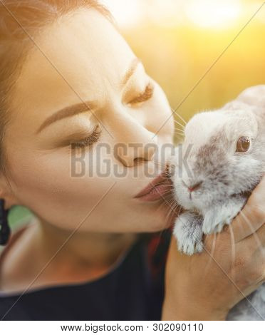Close-up Portrait Of Pretty Asian Kissing Little Fluffy Bunny On Summer Nature. Beautiful Girl Cares