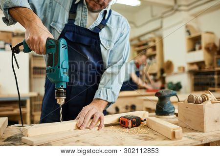 Closeup Of Mature Carpenter Drilling Wood While Working In Joinery, Copy Space