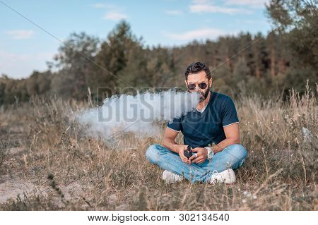 Stylish Vape Man Enjoying An Electronic Smoke Device Outside. Vaping Concept.