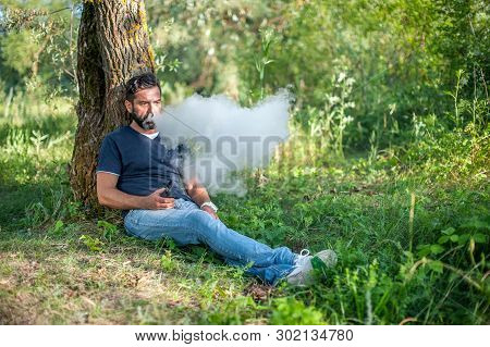 Modern Man Enjoying An Electronic Smoke Device Out In The Forest. Electronic Cigarette As Alternativ