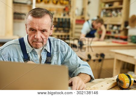 Portrait Of Senior Carpenter Using Laptop While Working In Joinery, Copy Space