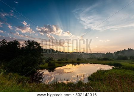 View Of A Sunset Rays Under The Forest Lake At The Meadow