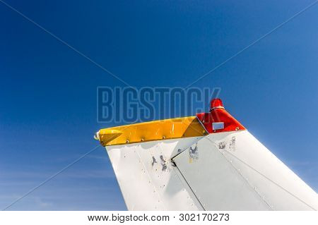 Tail Fin, Rudder And Beacon Lights, Small Single Engine Airplane With Old Paint And Bright Blue Sky.