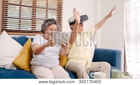 Asian Elderly Couple Using Tablet And Virtual Reality Simulator Playing Games In Living Room, Couple