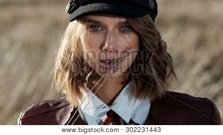 Portrait Of Attractive Female Model In Leather Jacket And Fashionable Cap Looking At Camera Against 