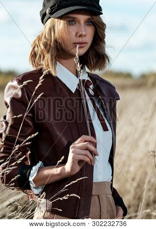 Portrait Of Attractive Female Model In Leather Jacket And Fashionable Cap Looking At Camera Against 