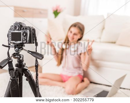 Young smiling videobloger teen girl is pointing at camera in living room