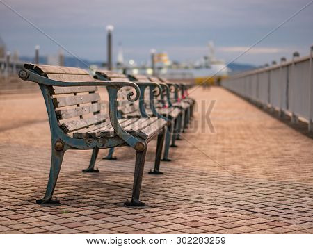 Wooden Benches Aligned In Line On The Pier With Boats At The Background