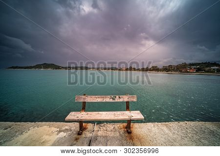 Empty Wooden Bench On A Concrete Pier With Stormy Dramatic Clouds Accumulating Over Alykes Bay In Za