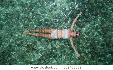 Aerial drone top view of woman floating in crystal clear sea water with coral reef